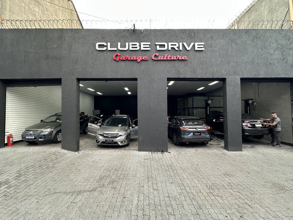 Fachada do Clube Drive na Água Branca: o letreiro Garage Culture sobre os quatro boxes abertos, com carros em atendimento e o pátio de bloquete na frente